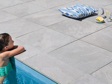 Une fillette s'appuie sur le bord de la piscine entourée de dalles imitation ardoise Alpine Grey