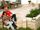 Couple assis sur une terrasse avec des dalles en travertin Medium SELECT et un mur en pierre naturelle, avec en arrière-plan des meubles de jardin en bois.