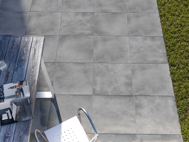 Vue sur une terrasse habillée de dalles effet béton Ombra, aperçu du gazon et du mobilier extérieur