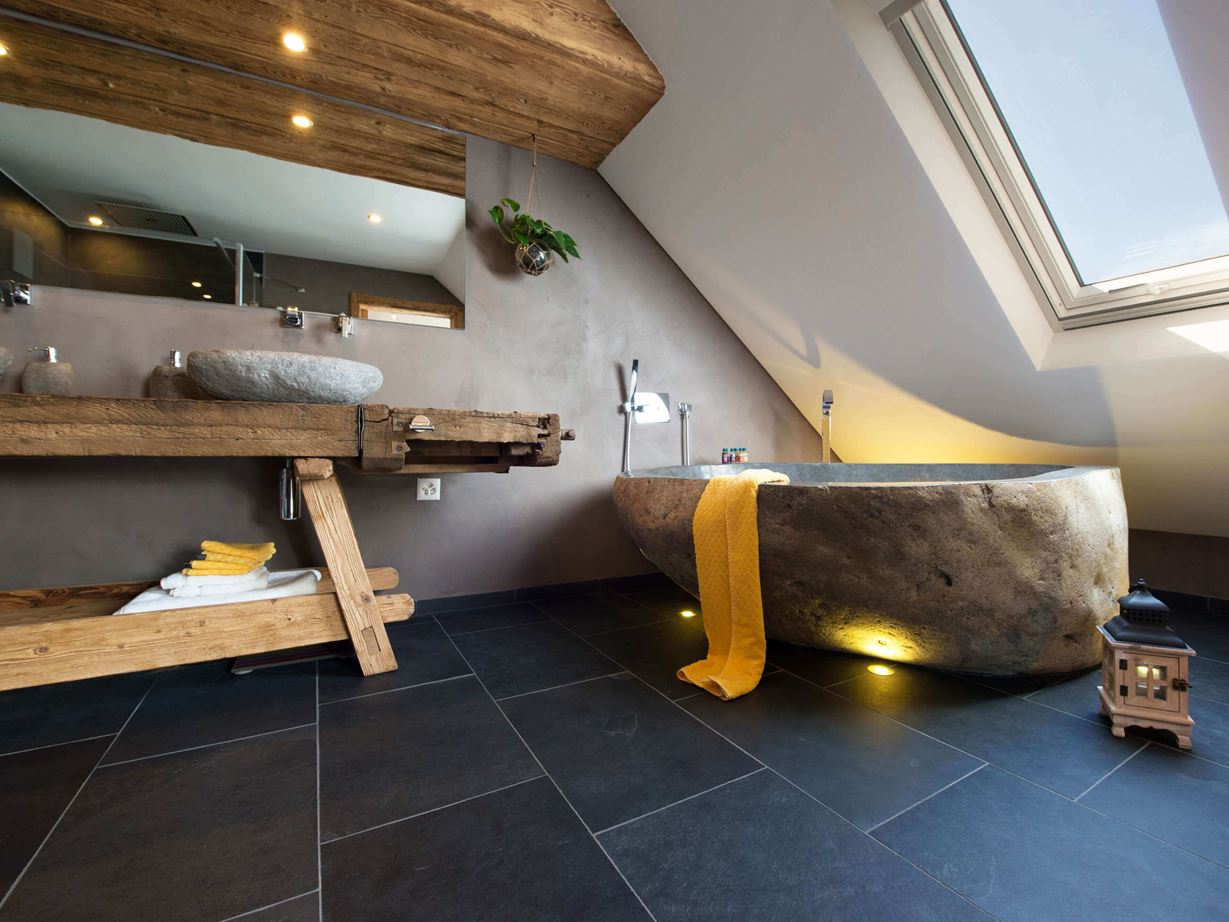 Salle de bain rustique avec baignoire en pierre et carrelage d'ardoise foncé comme revêtement de sol.