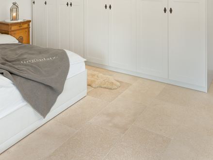Chambre avec armoire et lit blancs, et un carrelage en pierre calcaire beige au sol