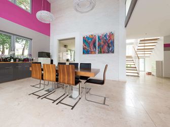 Salle à manger ouverte avec chaises modernes en bois et tableaux colorés au mur, rêvetement de sol en travertin clair à la surface adoucie