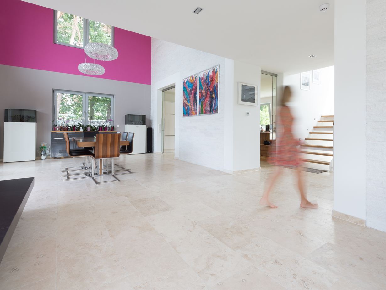 Salle à manger lumineuse avec des meubles modernes, des carreaux de travertin Classic Light lumineux comme revêtement de sol et un mur rose à l'arrière-plan.
