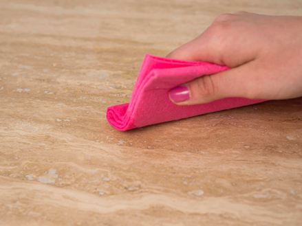 Hand wischt mit rosa Tuch über beigen Naturstein
