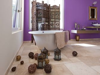 Carreaux de travertin Light dans une salle de bains avec baignoire autoportante et mur violet en arrière-plan