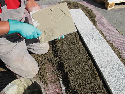 Verleger bestreicht die Rückseite des Steins mit Kleber für die Verlegung mit Einkornmörtel auf Schottertragschicht