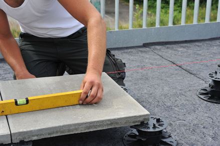 Les dalles sont posées sur pilotis, l'installateur utilise un niveau à bulle