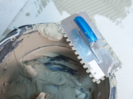 Un seau avec de la colle pour pierres naturelles et une truelle à dents