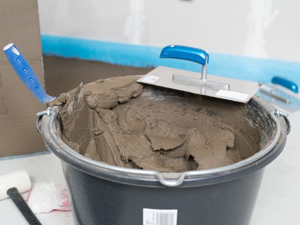 Un seau avec de la colle pour pierres naturelles et une truelle à dents