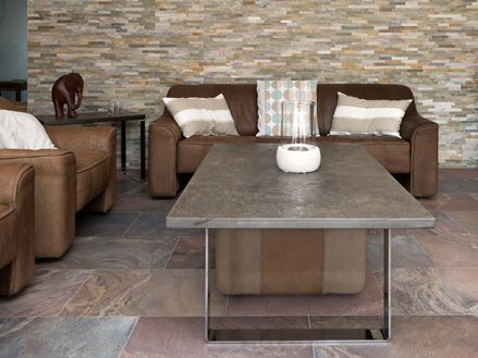 Wohnzimmer mit braunen Couchmöbeln, rötlichen Quarzitfliesen als Bodenbelag und Natursteinverblender an der Wand